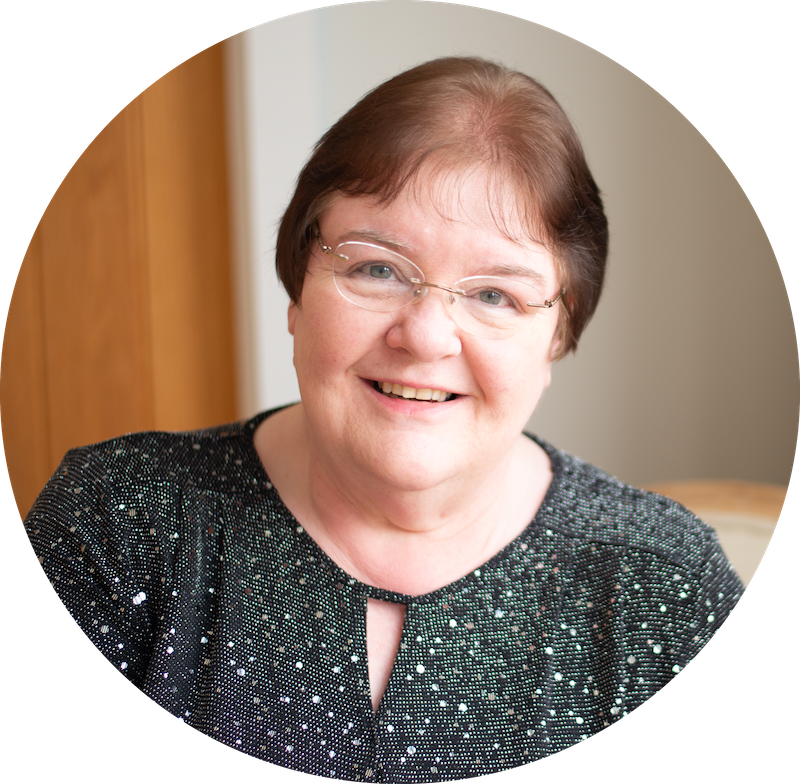A head and shoulders shot of Anne smiling. She has short brown hair and is wearing a black sparkly blouse.