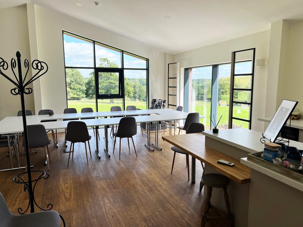 A picture of the function room, at the Deer Park, Hoar Cross.It shows a brown wooden floor, kitchenette to te right and chairs and a table in the background. There are two large windows.